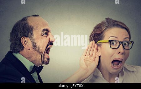 Can you hear me? Portrait angry man screaming curious surprised woman with glasses and hand to ear gesture listens isolated on grey wall background. H Stock Photo