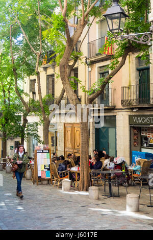 A woman walking along a street where diners are eating al fresco style in the old quarter of Girona, Spain. Stock Photo