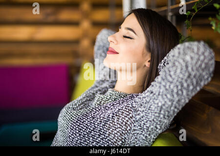 Cheerful young beautiful woman keeping hands behind head with smile while sitting at her working place Stock Photo