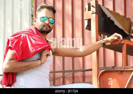 Young Indian man wearing fancy goggle with red shirt on shoulder looking at camera Stock Photo