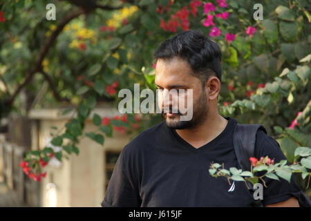 Young Indian man thinking looking down, with flowers in backdrop Stock Photo