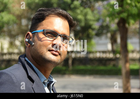 Young Indian corporate man with Bluetooth headset dreaming, thinking Stock Photo