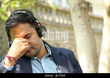 Young Indian corporate man listening to music closing his eyes in park Stock Photo