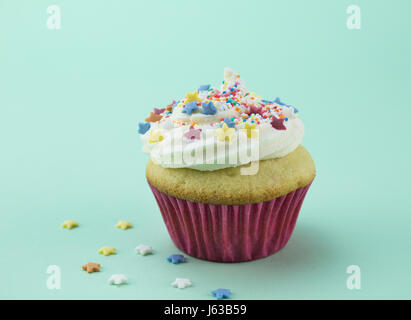 One vanilla cupcake with swirl white frosting sprinkled with star and ball candy colorful sprinkles against soft green background - space for text Stock Photo