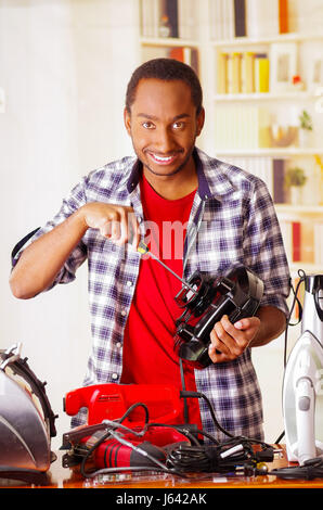 Happy Young African Ecuadorian smiling male Technician repairing a toaster with a screwdriver Stock Photo