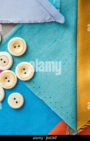 sewing, patchwork, tailoring and fashion concept - macro of desktop designer with white buttons and scraps of colored tissue, patches of blue, gray fabric, flat lay, top view, vertical. Stock Photo
