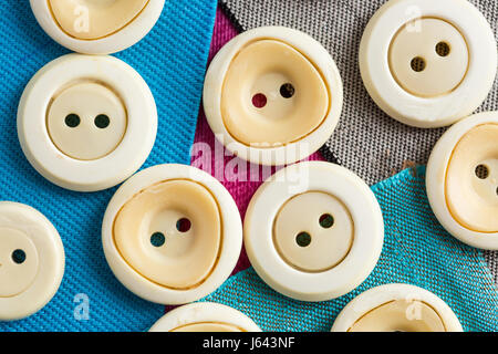 sewing, patchwork, tailoring and fashion concept - macro on beautiful white clothing buttons over background of blue, gray, purple flaps of textile fabric, flat lay, top view. Stock Photo