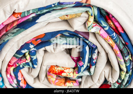 patchwork, sewing and fashion concept - macro of beautiful colorful quilted blanket is rolled up in a tube at studio, warehouse of finished products, side view. Stock Photo