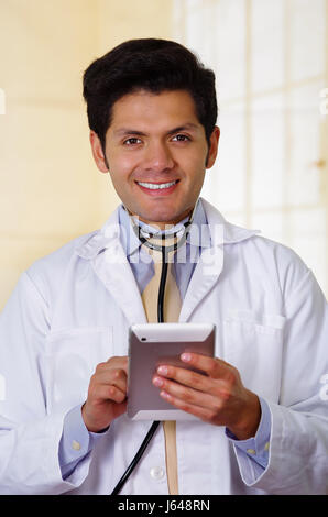 Handsome smiling doctor with an Stethoscope holding from his neck, writing on his notebook notes in office background Stock Photo