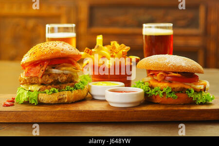 Two delicious hamburgers with beef, onion, tomato, lettuce and cheese with ketchup, mustard and two glasses of beer on wooden board Stock Photo