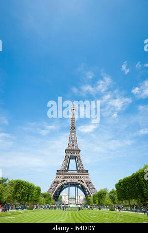 Bright daytime scenic view of the Eiffel Tower in Paris, France, with spring greenery on the Champs de Mars under clear blue sky Stock Photo