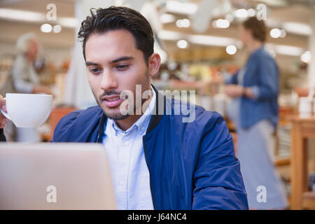 Young man drinking coffee at laptop in cafe Stock Photo