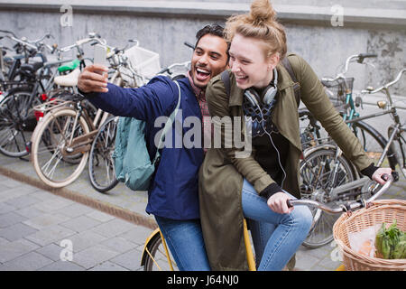 Playful, laughing young couple taking selfie with camera phone on bicycle Stock Photo
