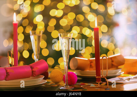 Champagne flutes, candles and Christmas crackers on dining table Stock Photo