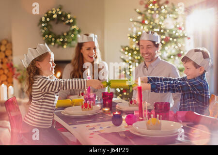 Family in paper crowns pulling Christmas cracker at dining table Stock Photo