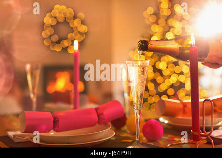 Pouring champagne into champagne flute on Christmas dinner table with Christmas cracker Stock Photo