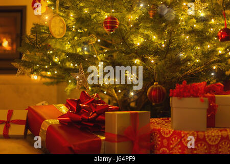 Gifts with red bows under illuminated Christmas tree Stock Photo