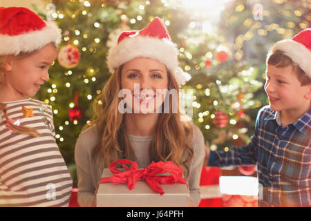 Portrait smiling mother in Santa hat receiving Christmas gift from daughter and son Stock Photo