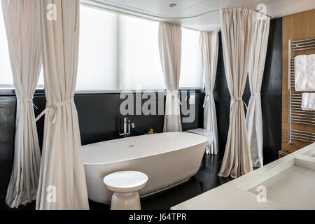 Heavy canvas curtains enclosing bath and shower set in dark honed stone. The basin and bath designer is Antonio Lupi Stock Photo