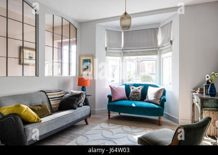 Large french metal salvaged windows in sitting room with grey vintage sofa from French Affair. The rug is by Allegra Hicks and the small sofa upholste Stock Photo