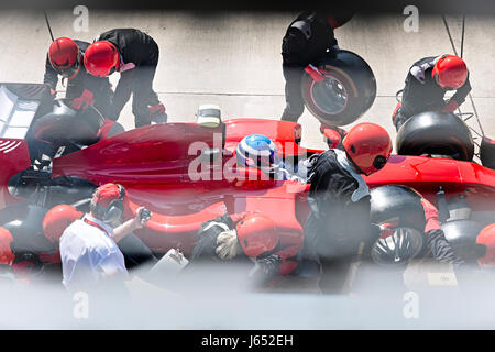 Manager with stopwatch timing pit crew replacing tires on formula one race car in pit lane Stock Photo