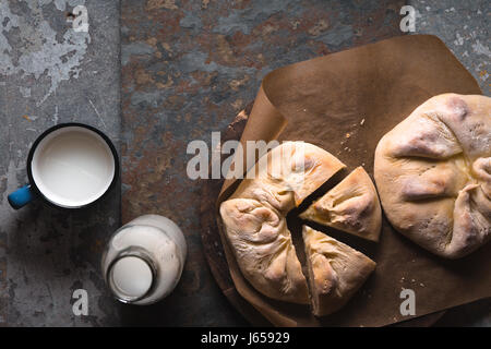 Ready-made khachapuri with cheese and pieces on parchment and milk in a bottle diagonal Stock Photo