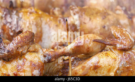 Many chickens cooking on a barbecue grill with slowly rotating spits, skewers. Stock Photo