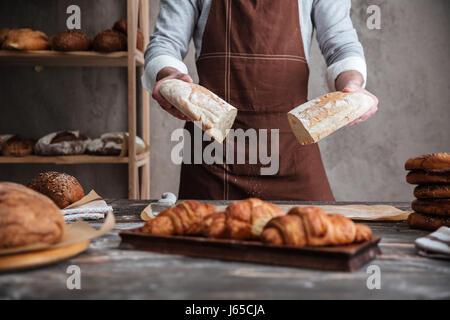 Cropped photo of young man baker standing at bakery holding bread. Stock Photo