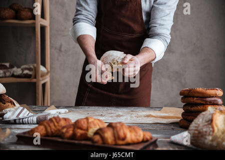 Cropped photo of young man baker standing near croissants holding bread Stock Photo