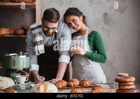Smiling woman looking camera while her man writing recipe of bread Stock Photo