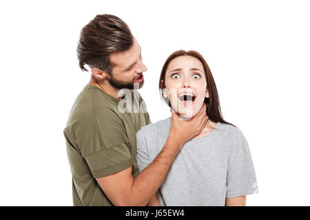 Image of offended young loving couple standing isolated over white background. Man strangling woman looking at camera. Stock Photo