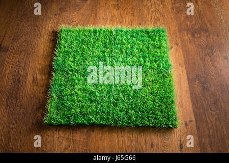 Green lush artificial grass tile on dark hardwood floor. Stock Photo
