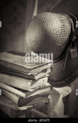 Pile of old books and straw hat with ribbon on a chair. Stock Photo