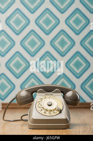 Vintage gray telephone on hardwood floor, diamond light blue retro wallpaper on background. Stock Photo