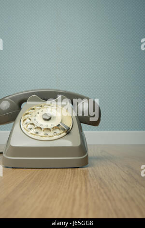 Gray vintage phone on hardwood floor and dotted light blue wallpaper on background. Stock Photo