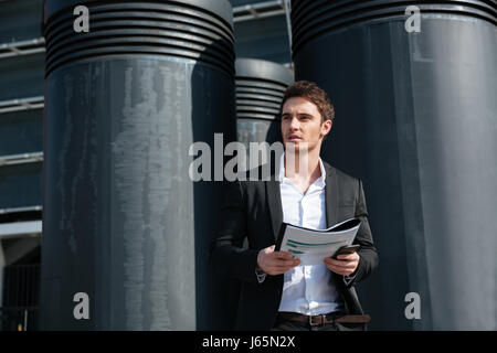 Serious handsome businessman holding documents and looking away in the street Stock Photo