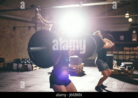 Side view of young man and woman lifting barbells in gym. Stock Photo