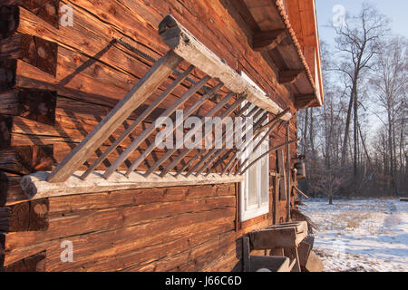 A wooden ladder hanging on a  wooden logs home illuminated by the light of the rising sun in  winter Stock Photo