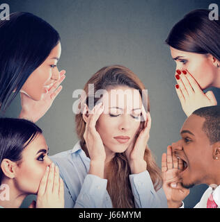 Group of young people whispering gossip to a stressed woman suffering from headache Stock Photo