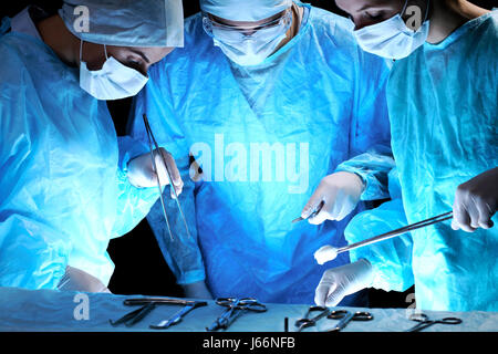 Medical team performing operation. Group of surgeon at work in operating theatre toned in blue Stock Photo