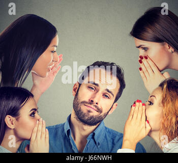 Four women whispering a secret latest gossip to a bored annoyed man Stock Photo