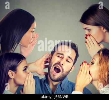 Four women whispering a secret latest gossip to a bored sleepy man Stock Photo