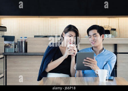 Young Asian couple surfing the web / looking at digital tablet in cafe. Social network and technology concept Stock Photo