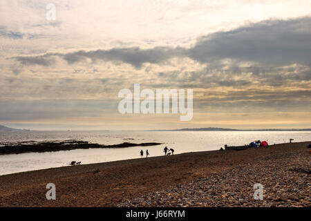 Distant figures silhouetted against the sea at sunset on the stony beach at Ringstead Bay, Dorset, UK Stock Photo