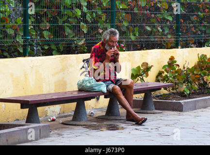 A homeless beggar on a street bench in Playa Las Americas catching a rest while the prosperous world passes him Stock Photo