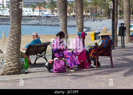 A group of West African sisters enjoy a well earned snack as the take a rest from their hair plaiting business for tourists on the promenade at Playa Stock Photo