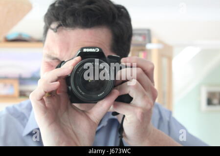 Man with black hair and blue shirt taking a self portrait photo in a mirror inside a house Stock Photo