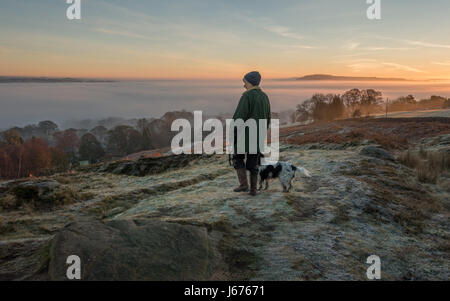 woman walking dog on a path on Ilkley Moor on a frosty early morning looking at countryside views of a cloud inversion, Wharfe valley, Yorkshire, UK Stock Photo