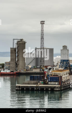 Napier, New Zealand - March 9, 2017: Large fuel tanks and silos at the commercial port under silver sky. Tugboat, light poles, containers and other ha