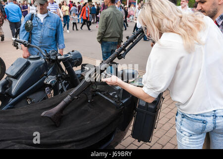 Russia, Moscow. Saturday, May 20, 2017. A show of vintage cars and motor cycles is under way in Sokolniki amusement park. About 200 cars and bikes are exposed in the open air, including many Soviet made cars and automobiles from Sweden, Germany, USA, Japan and other countries of the world. A lot of people visit the exhibition despite the outcast day. Unidentified, unrecognizable woman touches a machine gun of the WWII period, mounted on a military motor cycle. Credit: Alex's Pictures/Alamy Live News Stock Photo